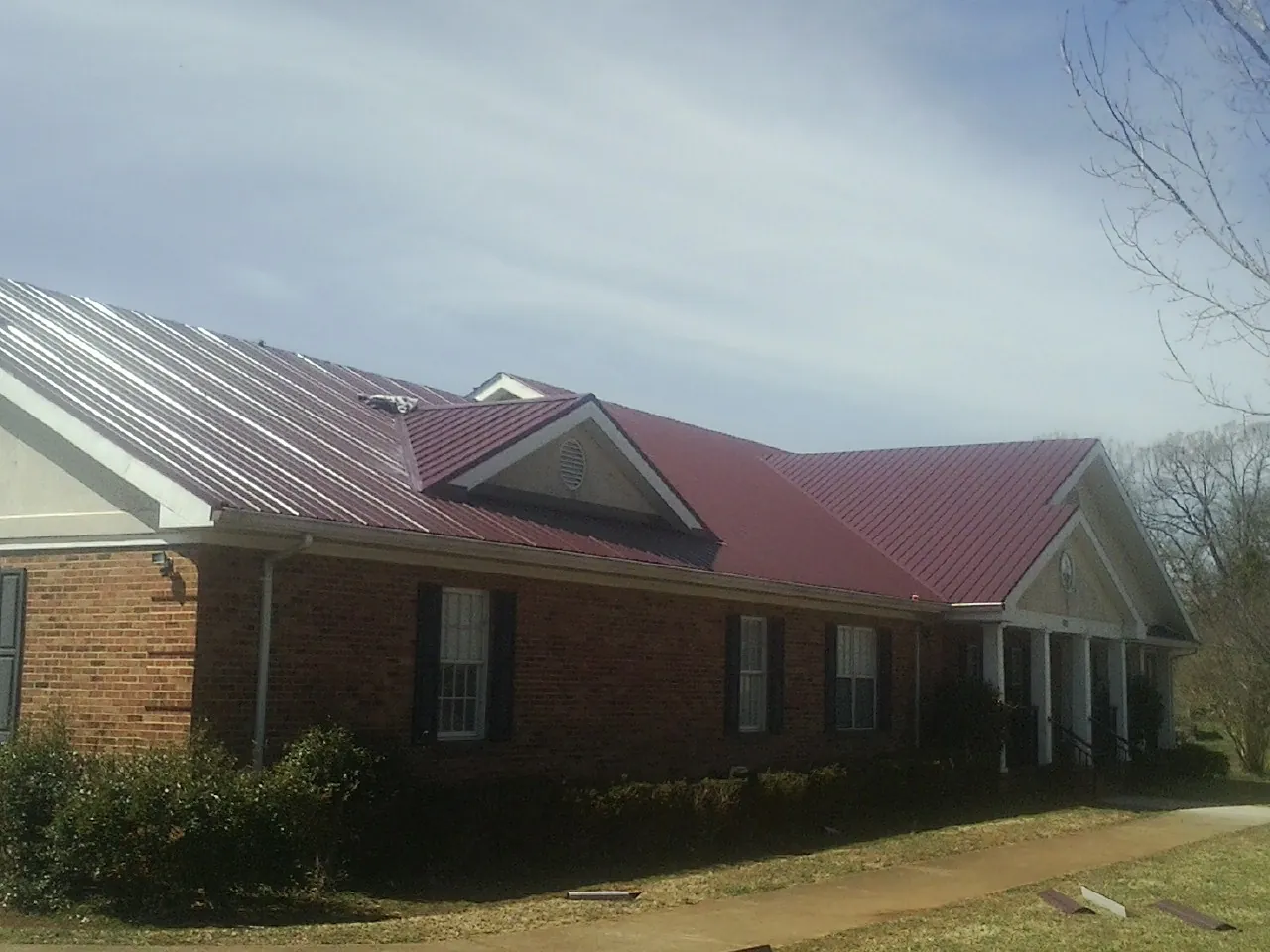 Red metal roof with gabled entries on a long brick building, from a Hail Damage Roof Repair job in Camp Grove