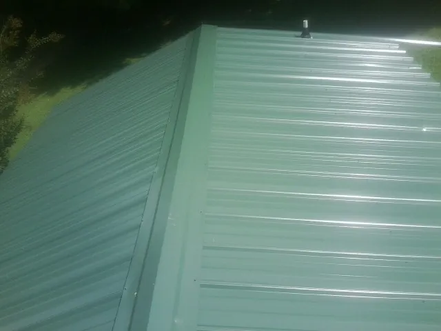 New green metal panels meeting at the ridge of a roof — Flat Roof Repair work by our crew in Camp Grove