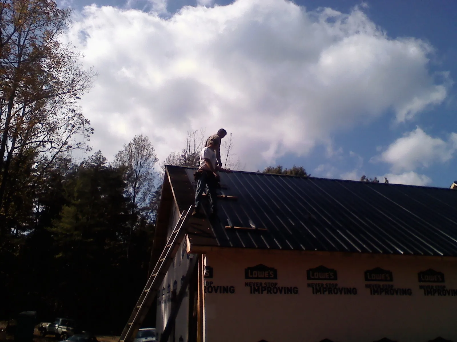 Roofer fastening dark metal panels high against a cloudy sky, from a Roof Inspection job in Camp Grove