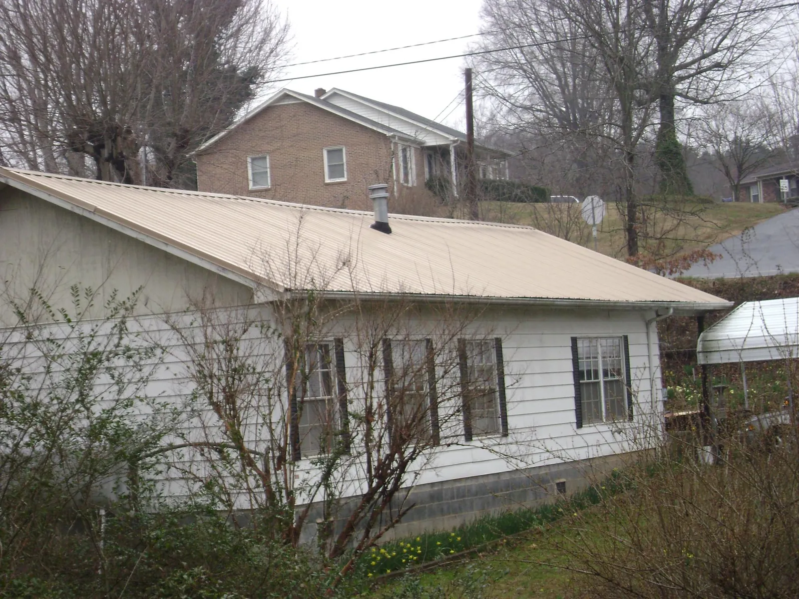Tan metal roof on a white sided house set into a hillside — Commercial Roofing by Roofing Brothers in Camp Grove