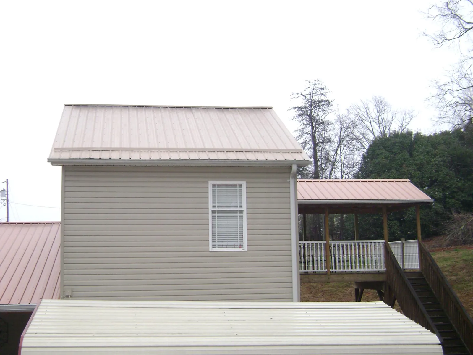 Tan metal roofs on a two story addition and attached porch, from a Roof Replacement job in Camp Grove